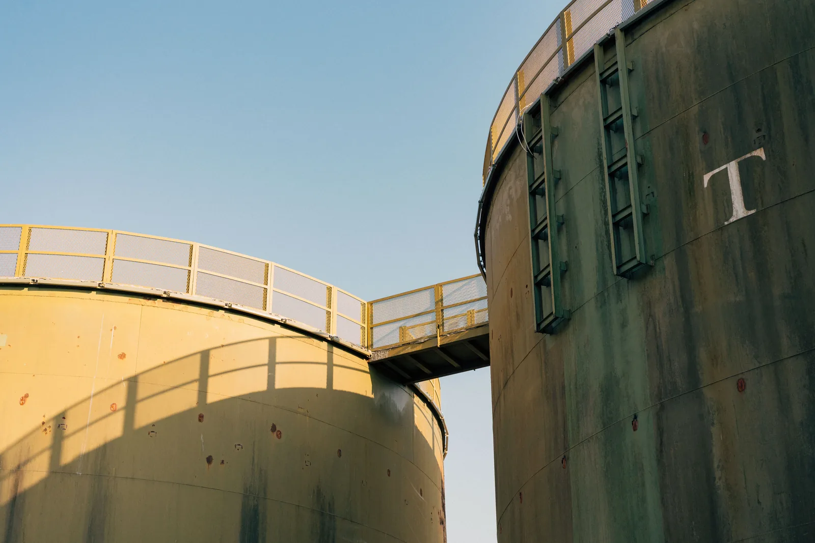 Industrial storage tanks connected by an elevated maintenance walkway
